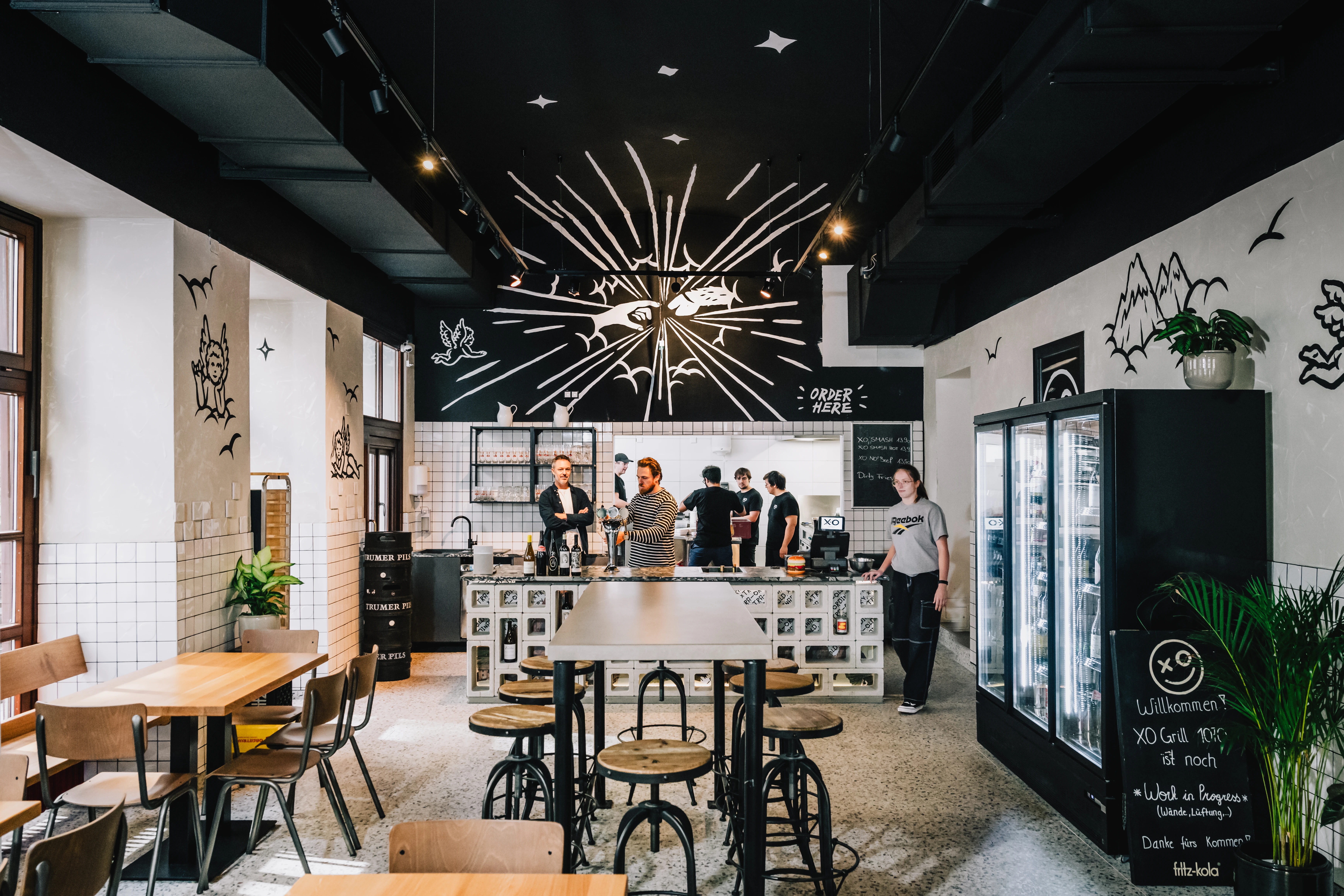 Innenansicht eines modernen Restaurants mit Bar, Tischen und Wandmalereien.